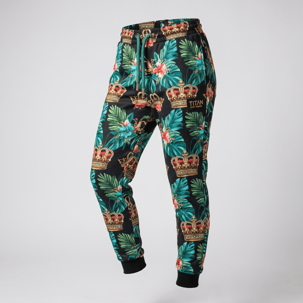 Black sweatpants featuring a tropical leaf and crown pattern with green drawstrings and a brand patch.