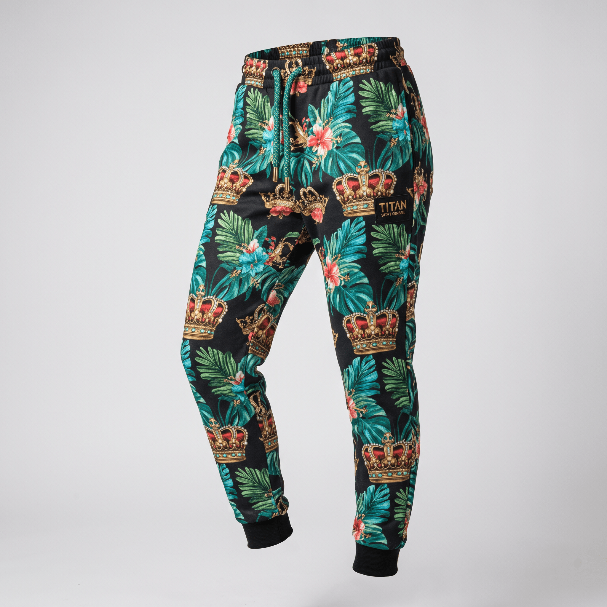 Black sweatpants featuring a tropical leaf and crown pattern with green drawstrings and a brand patch.