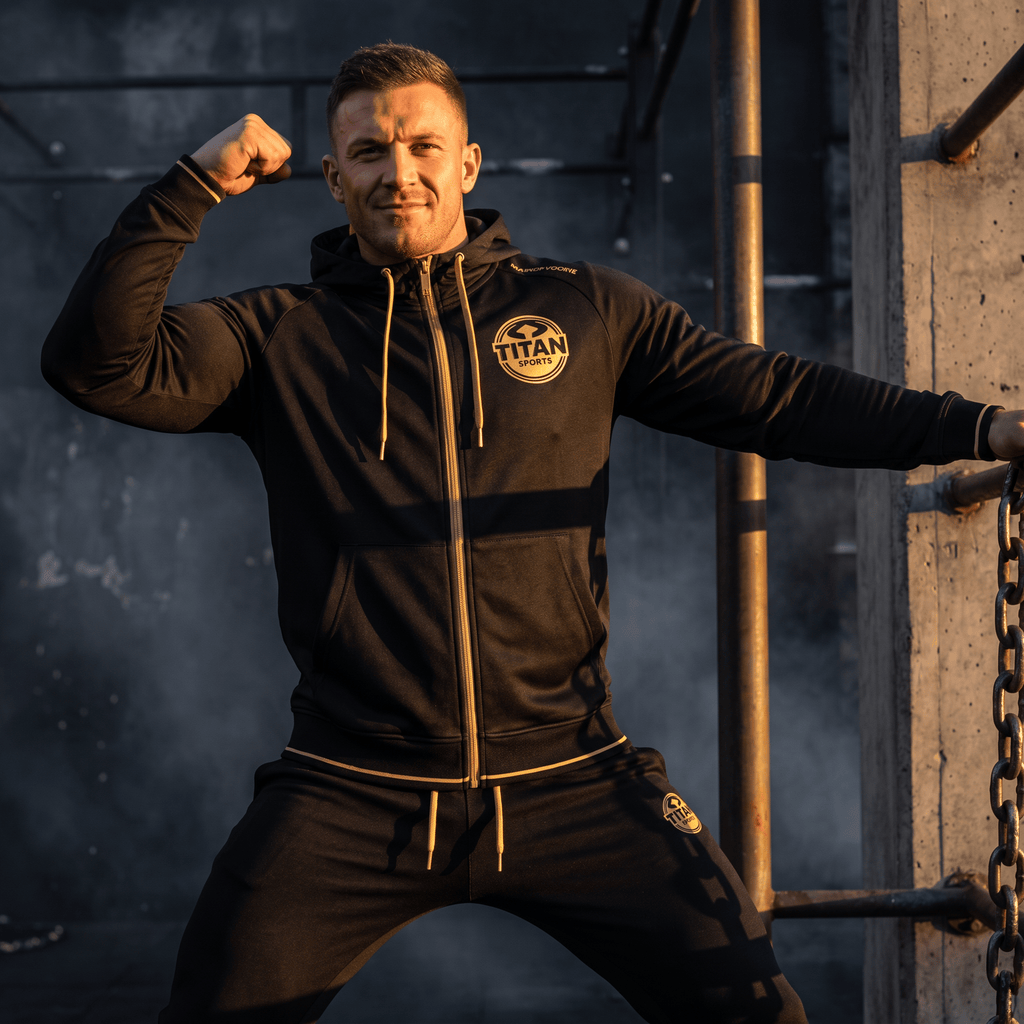 An athletic man flexes his bicep wearing a black TITAN warmup hoodie with gold accents.