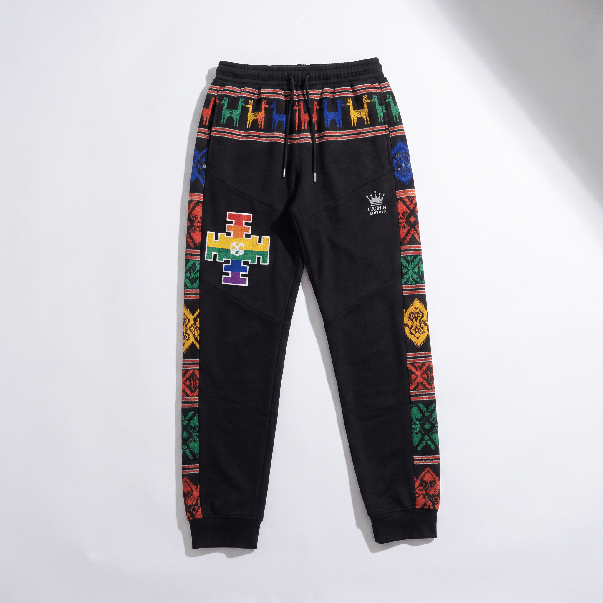 Black sweatpants with colorful patterned side stripes, a waistband llama print, and a rainbow cross patch.