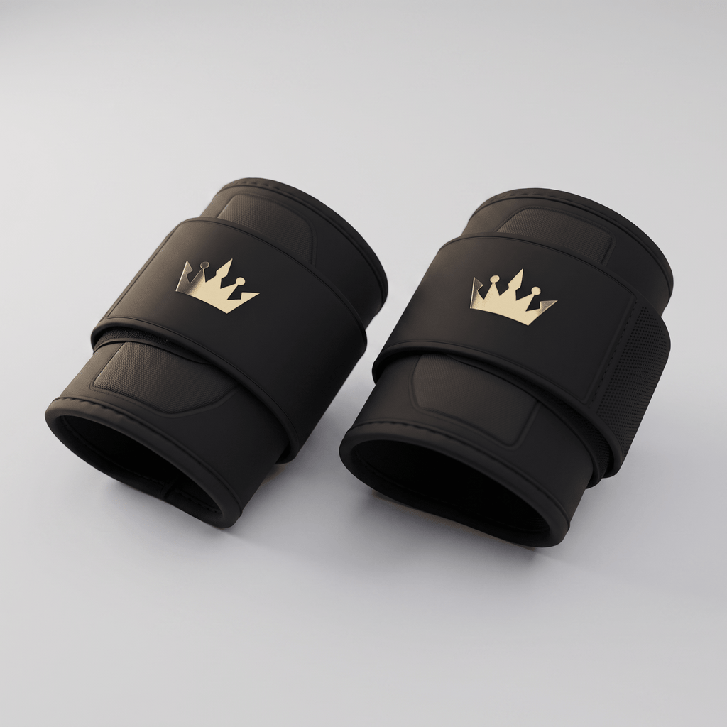 Pair of black weightlifting wrist wraps with gold crown logos on a light gray background.