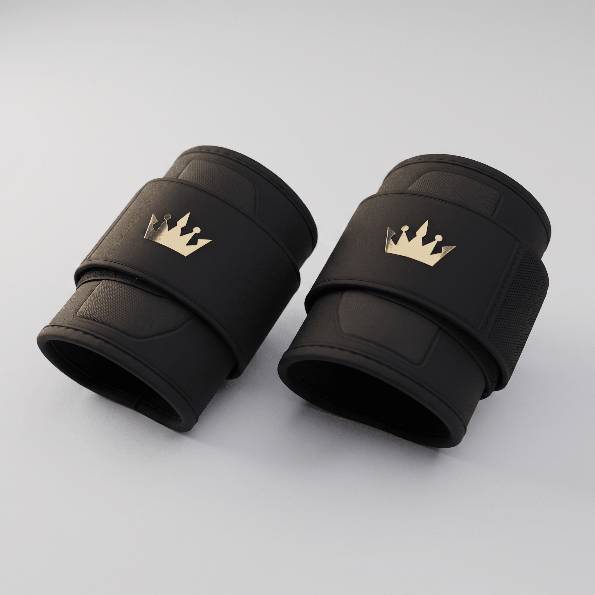 Pair of black weightlifting wrist wraps with gold crown logos on a light gray background.