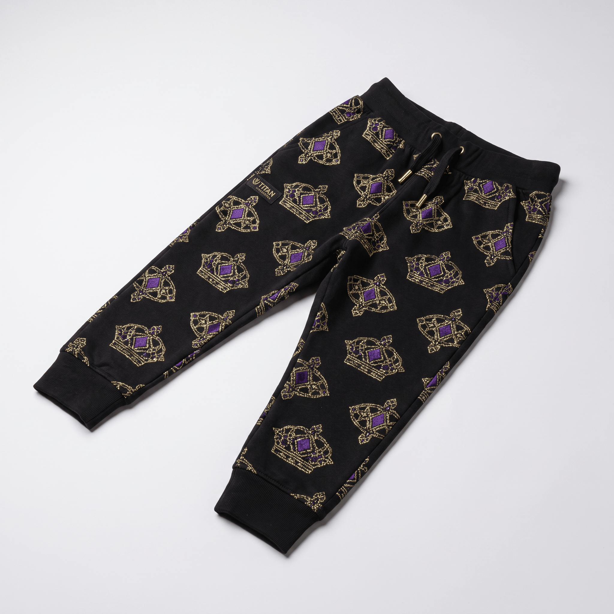 Black sweatpants with gold and purple crown pattern, elastic waistband, and cuffed ankles laid flat.