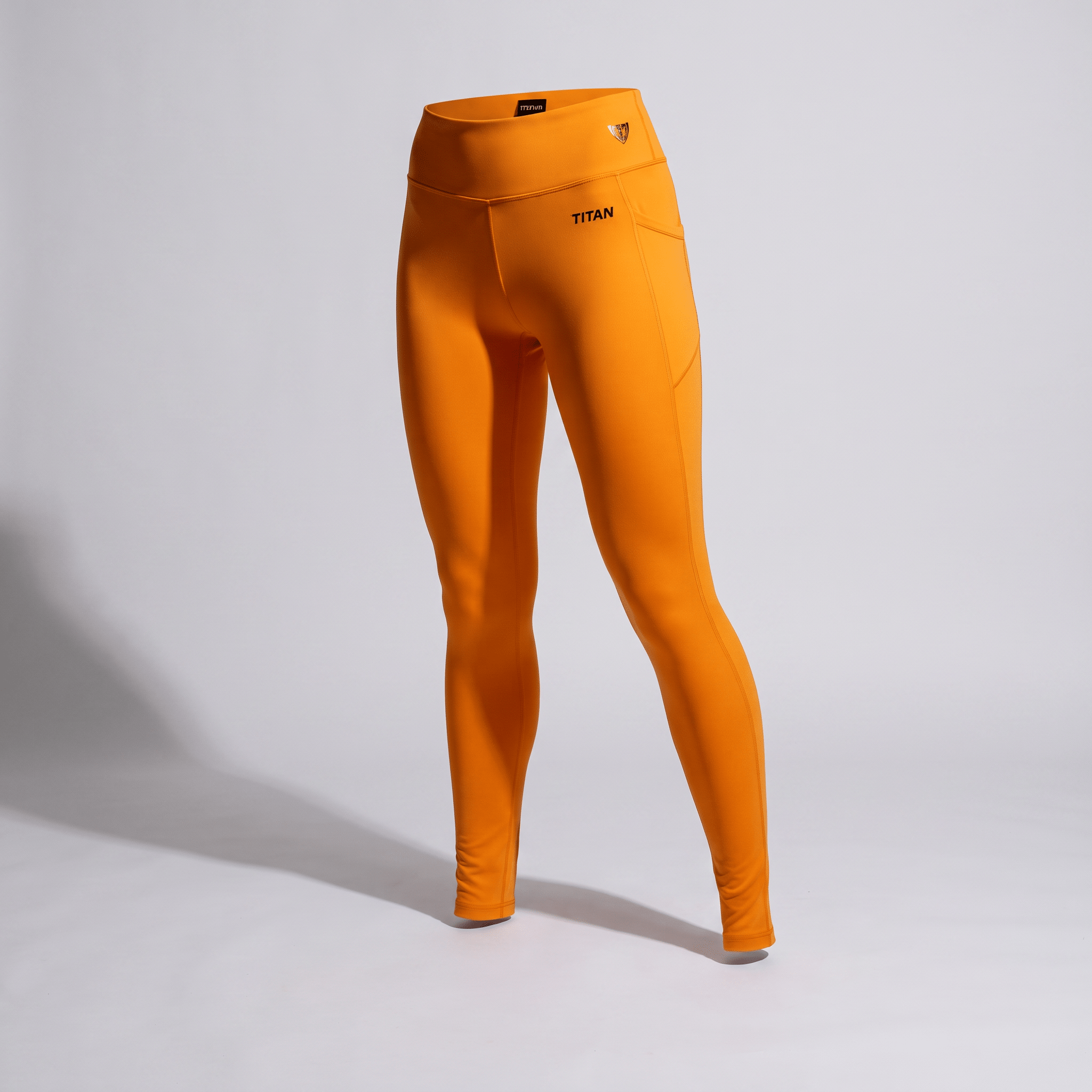 Bright orange high-waisted athletic leggings with side pockets and a Titan logo on a neutral background.