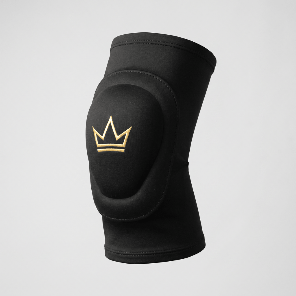 Black athletic knee pad with thick padding and embroidered gold crown logo on grey background.
