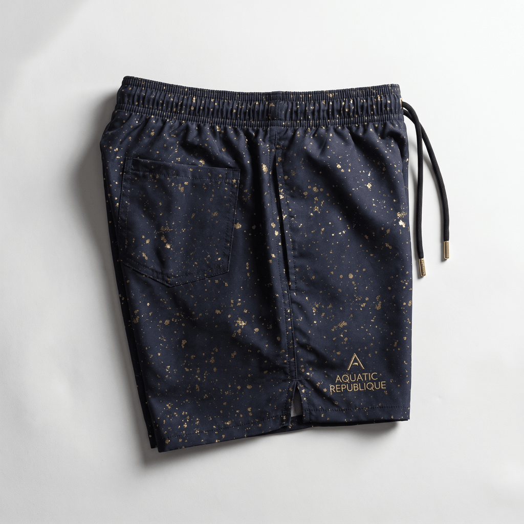 Navy blue swim shorts with gold paint splatter pattern, back pocket, and Aquatic Republique logo.