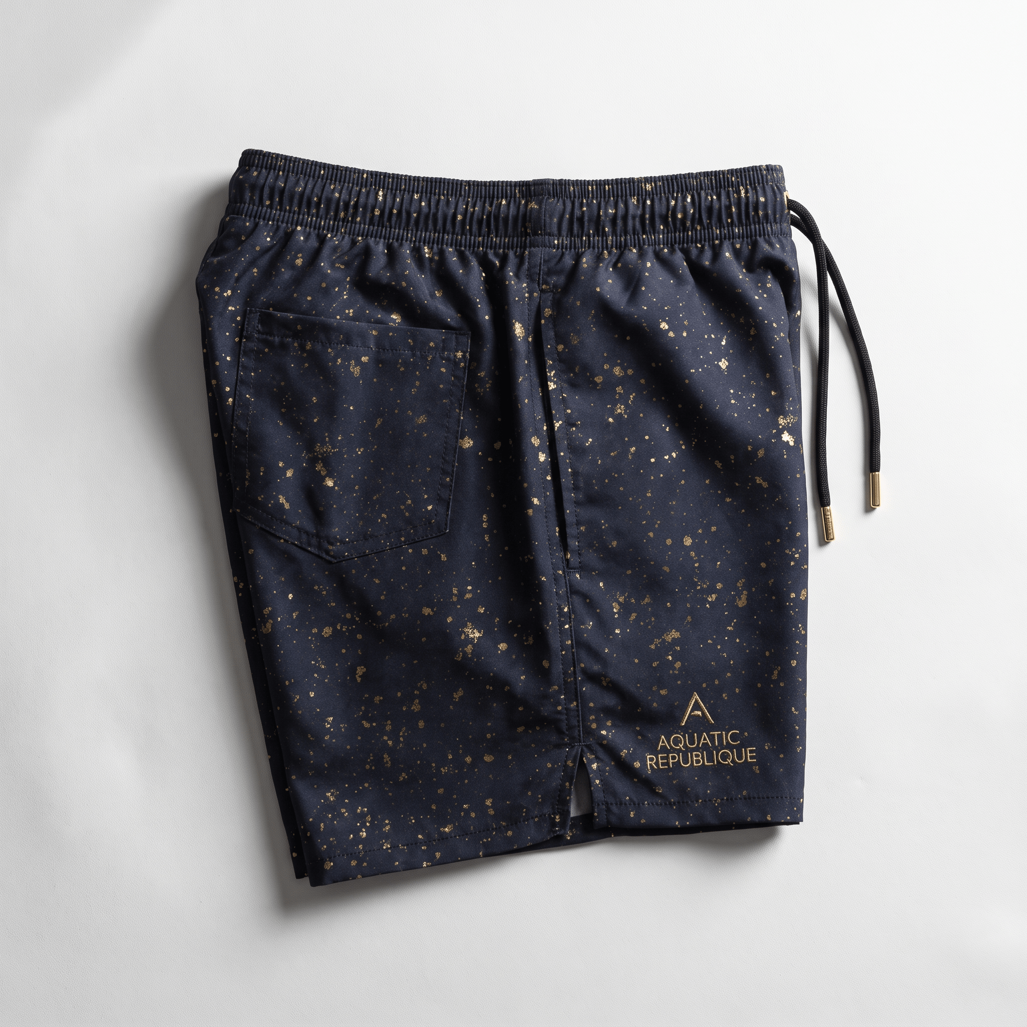 Navy blue swim shorts with gold paint splatter pattern, back pocket, and Aquatic Republique logo.