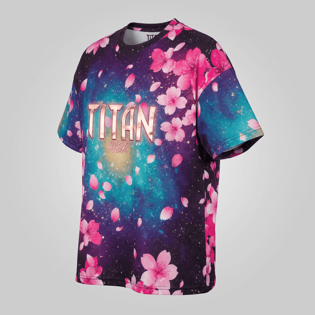 Black crewneck t-shirt with cosmic purple and teal galaxy print, pink cherry blossoms, and gold TITAN HER text.