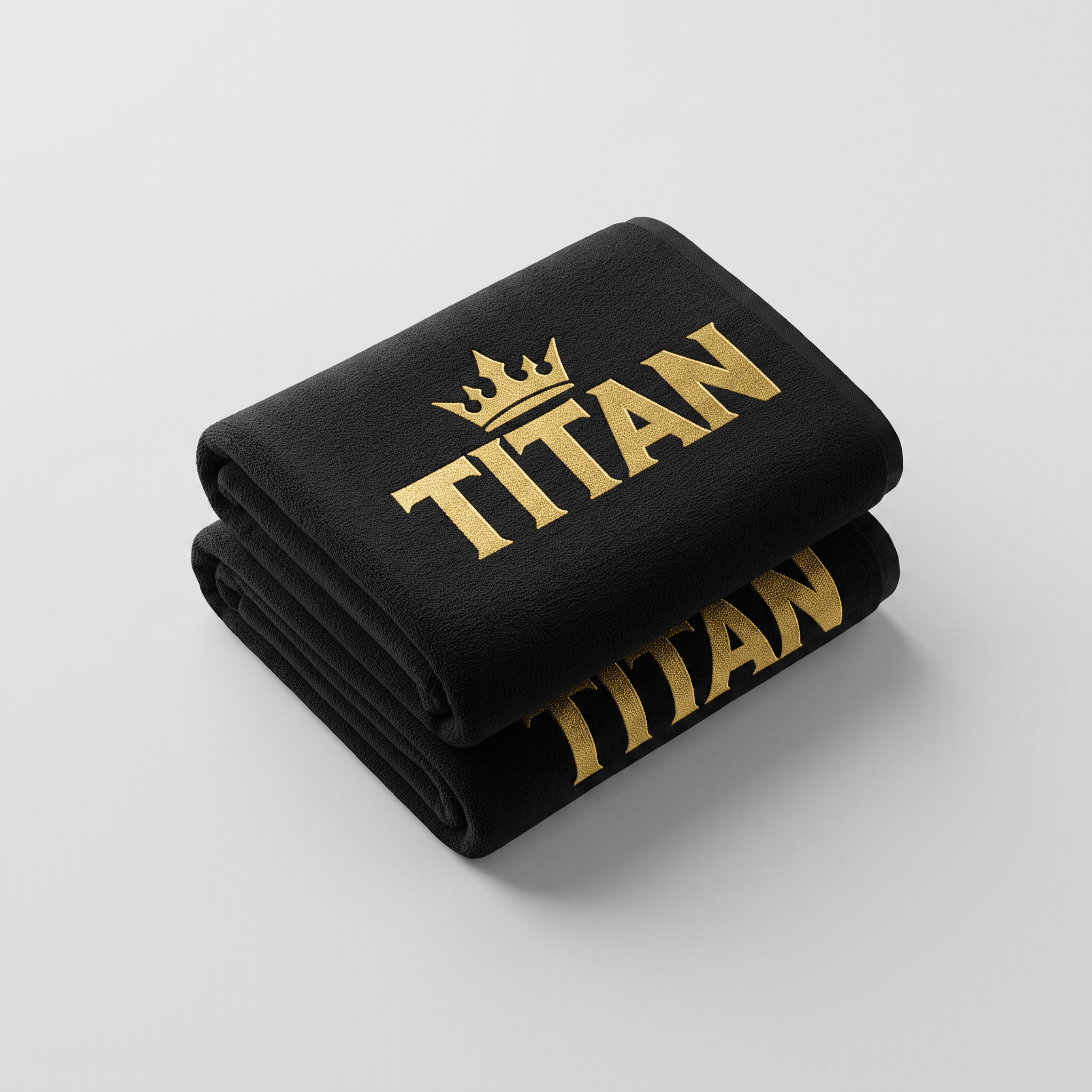 Folded black towel with embroidered gold crown logo and Titan text on a light gray background.