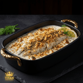 White fish in creamy sauce topped with pine nuts and herbs, served in a black baking dish with gold handles.