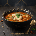 Steaming Bosnian fish stew in a black, gold-rimmed crown bowl, served with a gold spoon on a dark wooden surface.