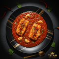 Two fish fillets in vibrant red Chraimeh sauce with garlic and chili, served on a black plate with gold accents.