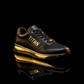 TITAN black low-top sneaker featuring gold "TITAN" logo, metallic gold midsole, and black mesh panel on black background.