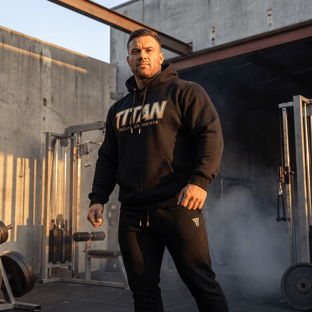 An athlete stands in a gym, posing in a black TITAN Youth Hoodie Future Champions with matching pants.