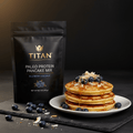 TITAN Paleo Protein Pancake Mix Blueberry Coconut — bright breakfast lifestyle shot with fluffy pancake stack, fresh blueberries and coconut flakes