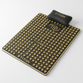 Black acupressure mat and pillow set with gold geometric accents, branding, and numerous gold massage spikes.