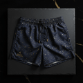 Navy swim shorts with gold paint splatter print, elastic drawstring waist, and gold Aquatic Republique logo on hem.