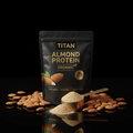 Black pouch of TITAN organic almond protein with gold text, scoop of tan powder, and scattered almonds on black surface.