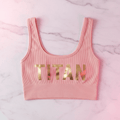 Pink seamless ribbed crop top with a scoop neckline and metallic gold "TITAN" logo on a marble background.