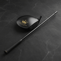 Matte black Titan Crown Edition golf swing trainer with gold crown logo on textured slate background.