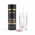 Black and gold tube of TITAN berry electrolyte tablets next to a glass of water with a dissolving pink tablet.