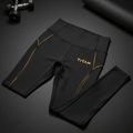 Black high-waist Titan leggings with gold accent piping and logo, displayed on a gym floor with weights and a mat.