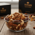 Clear bowl of TITAN Organic Trail Mix with dates, cashews, almonds, walnuts, and raisins on a wooden table.