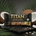 TITAN black and gold Coconut protein bar packaging with a clear window revealing the bar, set against split coconuts.