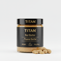 A black jar of TITAN Peanut Butter with gold text and a flexing arm icon, sitting next to a pile of whole peanuts.