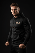 Man wearing a black TITAN hoodie with gold chest logo, hood drawstrings, and front kangaroo pocket.
