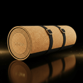 Rolled cork and black rubber TITAN Pro yoga mat with gold-toned buckled straps, isolated on a reflective black surface.