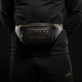 Black leather Titan Stealth fanny pack with gold zippers and raised gold logo, worn around the waist.