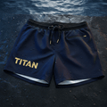 Navy TITAN quick-dry 7-inch swim trunks with black elastic waistband, gold logo, drawstring, and zip pocket.
