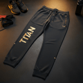 Charcoal tapered Titan training joggers with gold leg logo, zippered pockets, drawstring waist, and ribbed cuffs.